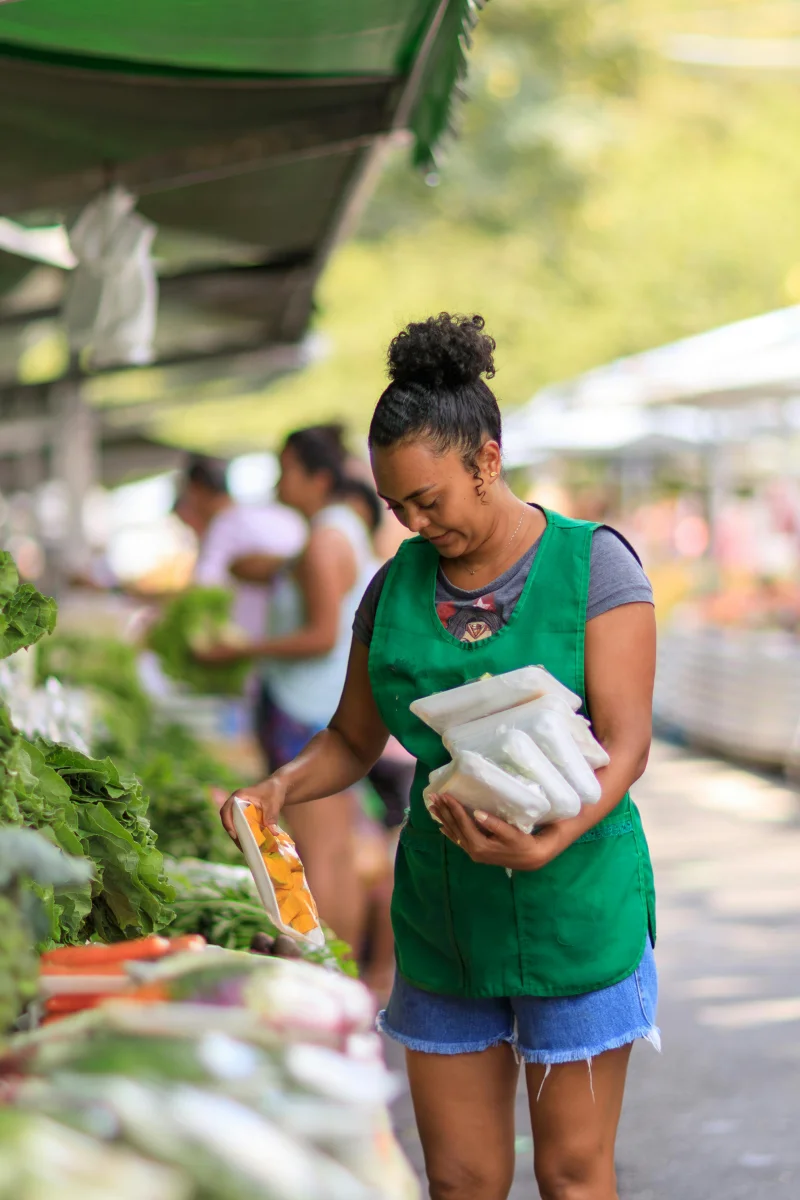 A woman selecting fresh vegetables at an outdoor farmers market on a sunny day.