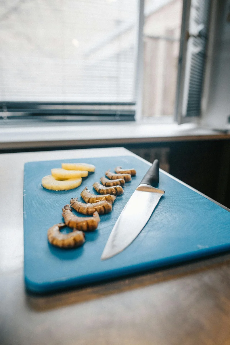 Close-up of shrimps and pineapple slices on a blue chopping board with a knife in a kitchen.
