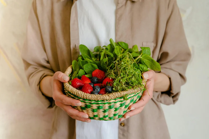 Close-up of a person holding a basket of strawberries, blueberries, and greens.