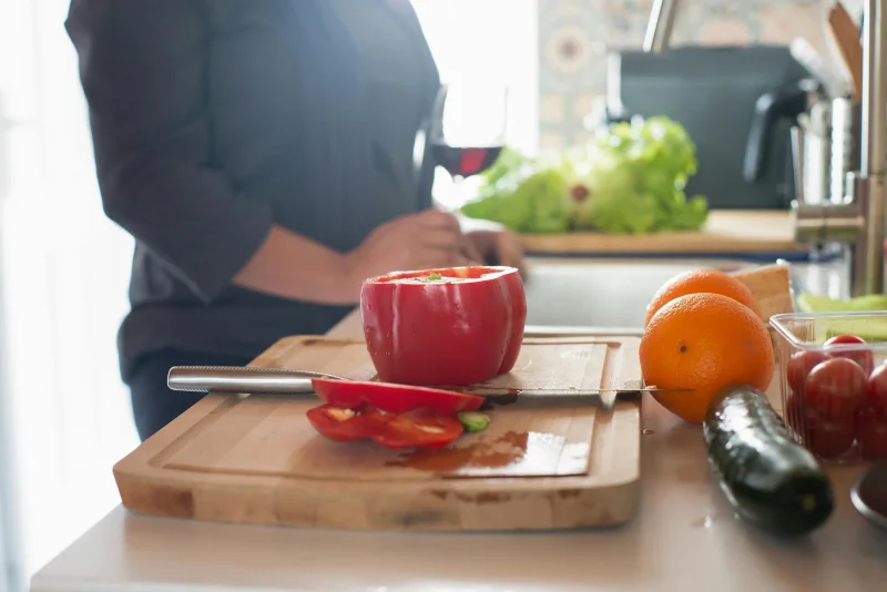 A vibrant kitchen scene with fresh produce including peppers, oranges, and cucumbers on a wooden chopping board.