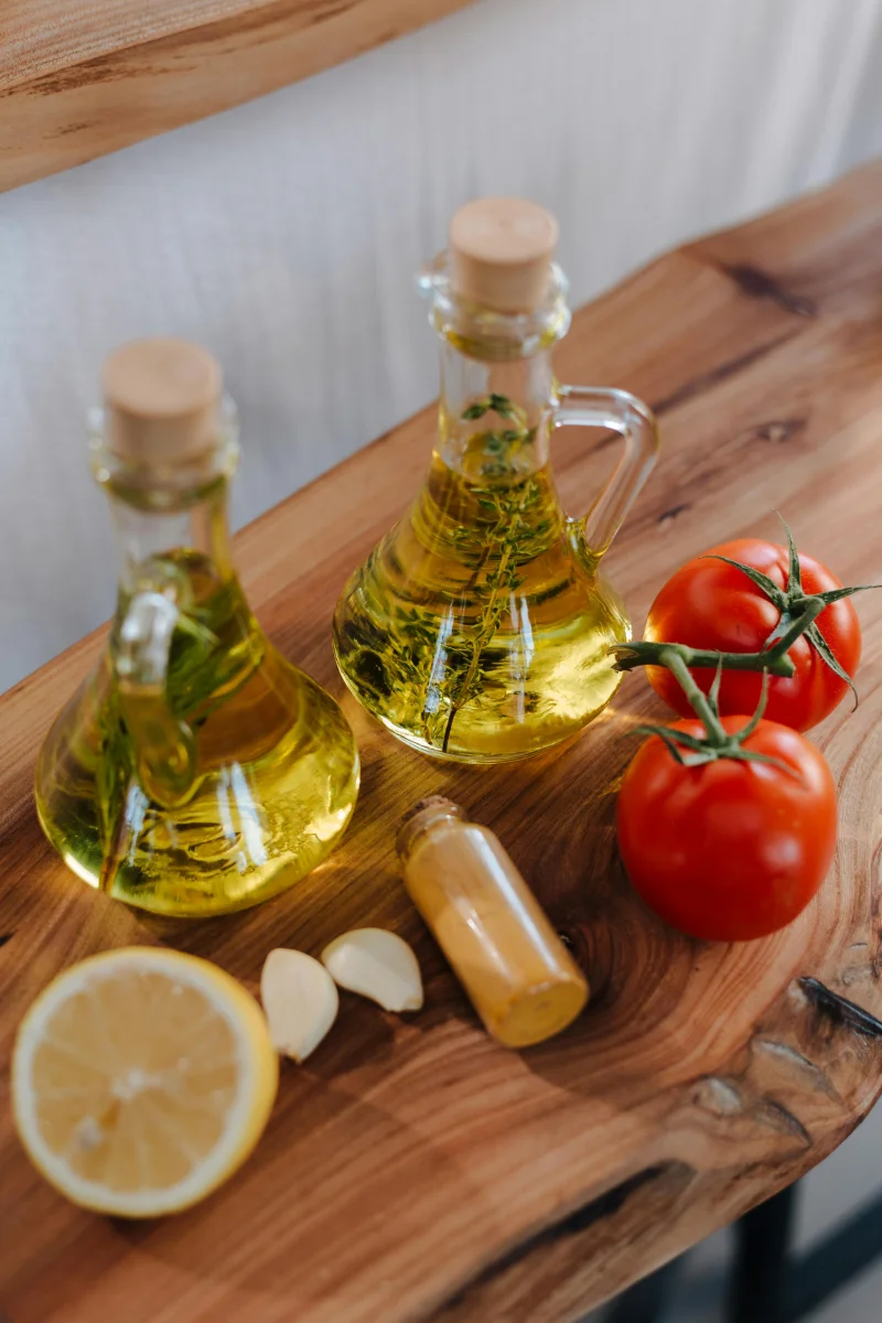 Fresh Italian ingredients including olive oil, tomatoes, garlic, and lemon on wooden surface.