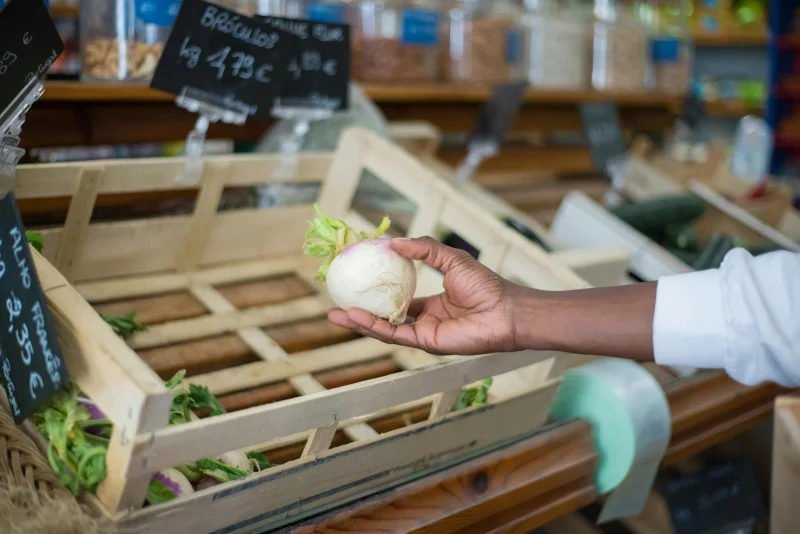 Close-up of a hand selecting a fresh turnip in a wooden crate at a Portuguese market.