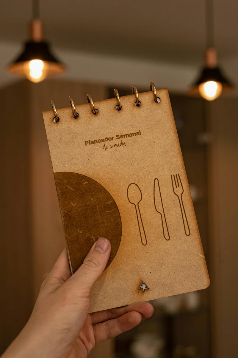 Close-up of a hand holding a rustic meal planner notebook indoors.