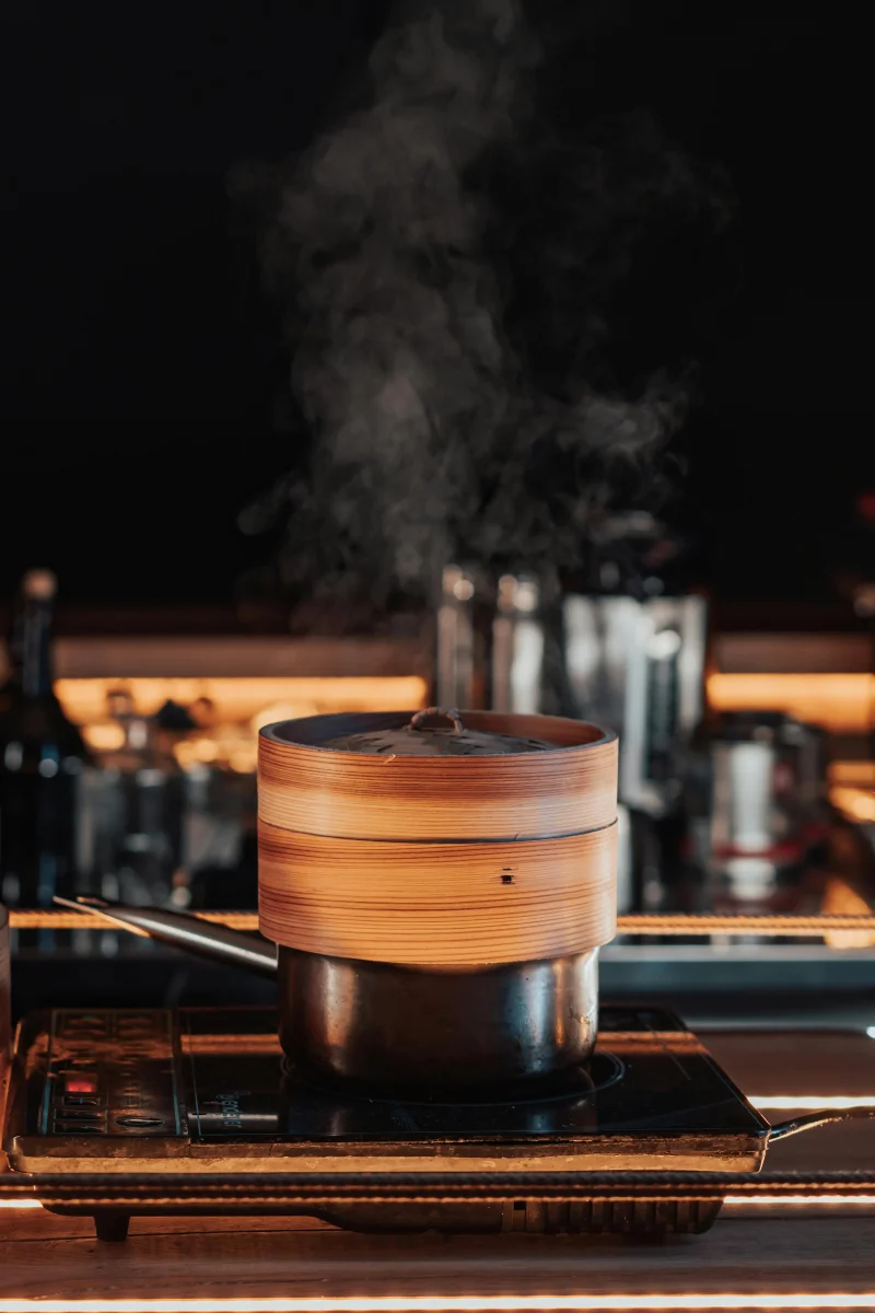 A bamboo steamer releasing steam on a stove, capturing a cooking moment.