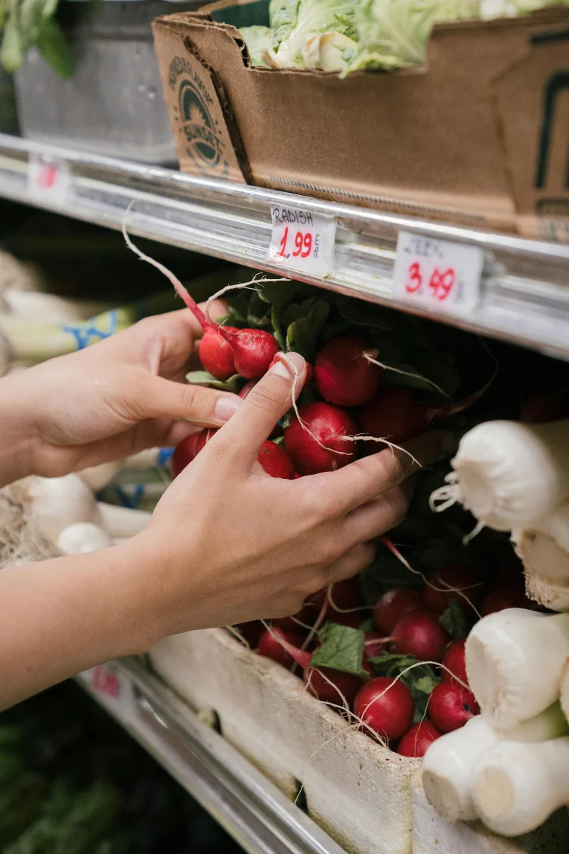 Close-up of hands selecting fresh radishes from a store shelf, showcasing organic produce.