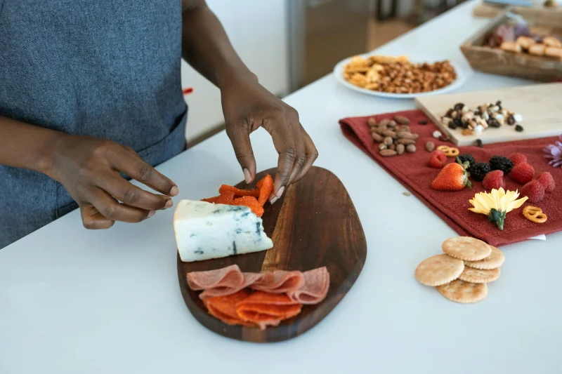 Close-up of hands assembling a charcuterie board with cheese, meats, and fruits. Perfect for culinary inspiration.