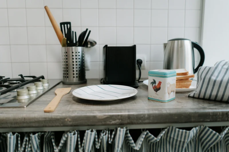 A clean kitchen counter featuring utensils, a kettle, and a tin can with vibrant design.