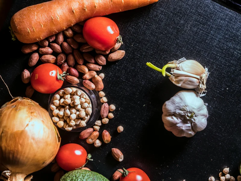 Top view of fresh vegetables and nuts arranged on a dark surface, showcasing raw ingredients.