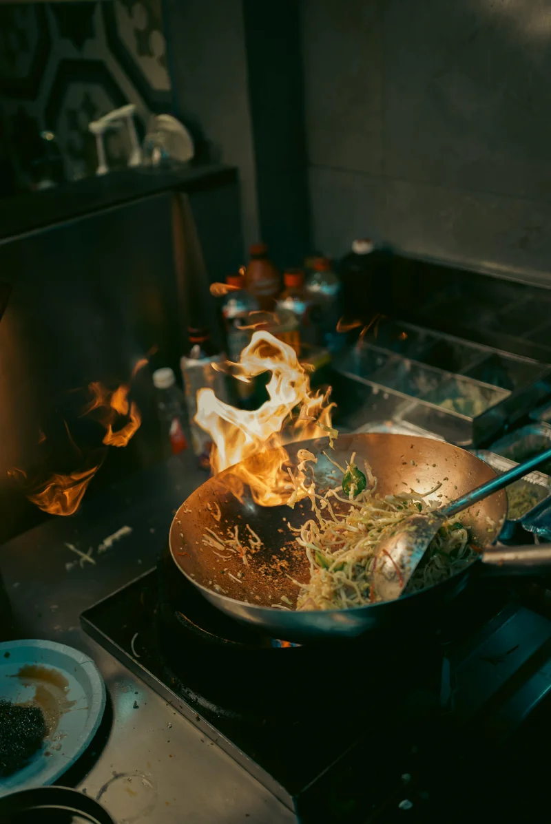 Exciting kitchen scene with stir-fried noodles in a fiery wok capturing culinary action.