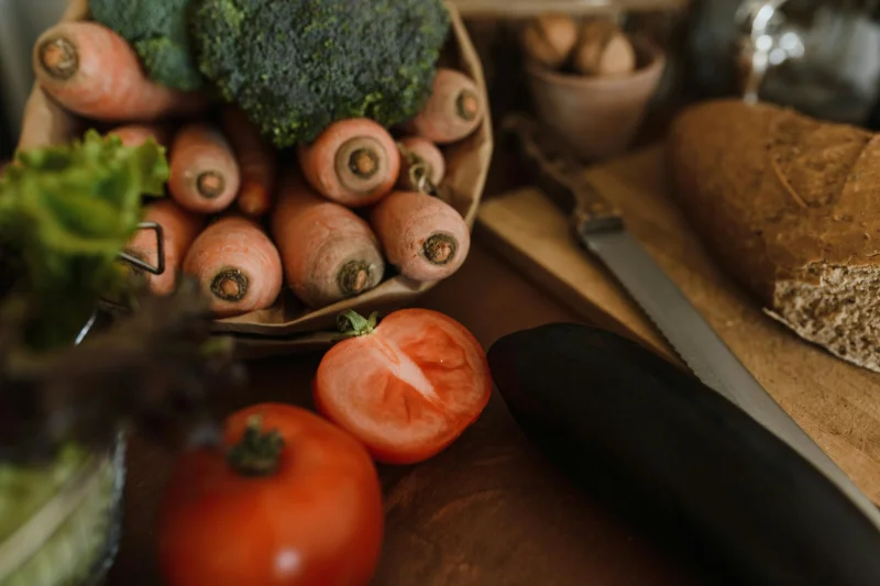 A vibrant assortment of organic vegetables with bread on a wooden table, showcasing healthy eating.