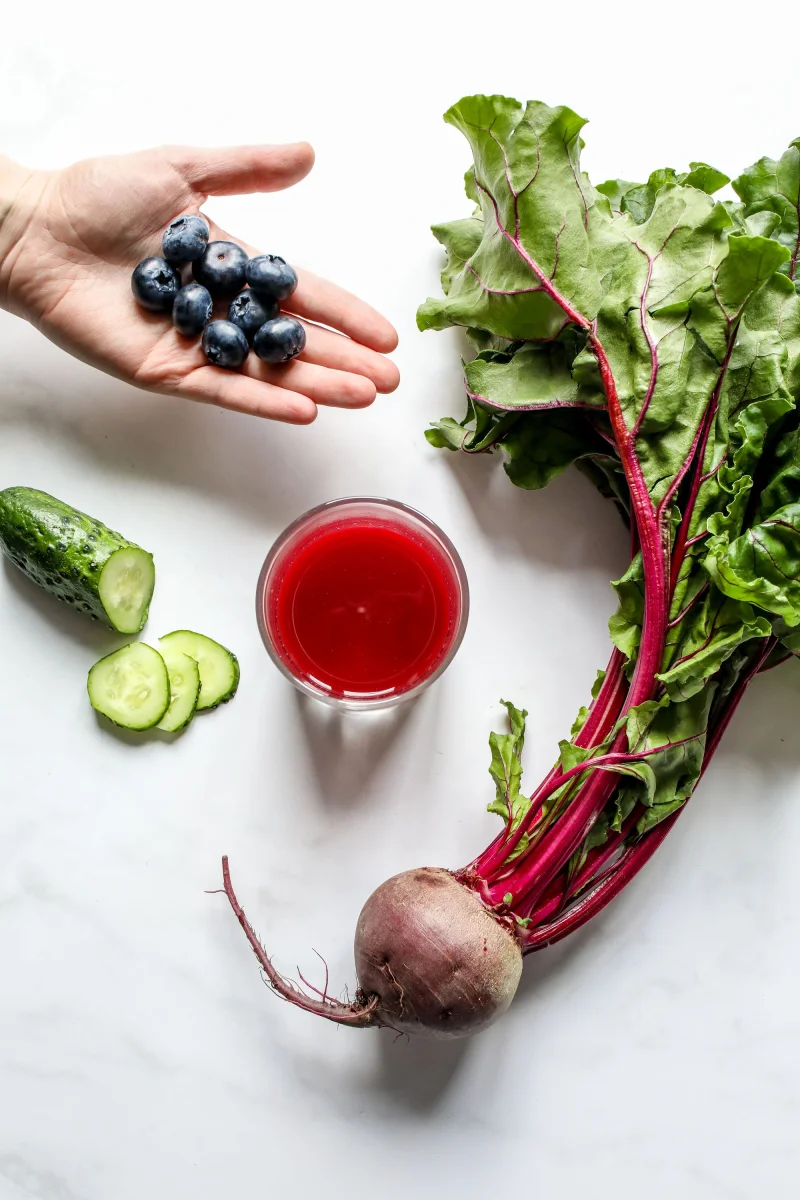 Top view of fresh beet juice with blueberries and cucumber on a white background.