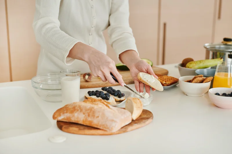 Woman spreads cream on bread with blueberries. A wholesome breakfast setup.