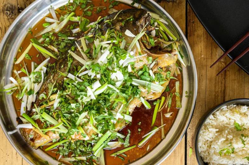 A flavorful steamed fish dish garnished with herbs, served with rice.