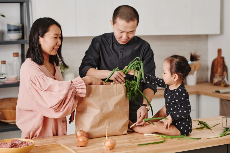 A family enjoys unpacking groceries together on a wooden kitchen table, sharing moments of fun and bonding.