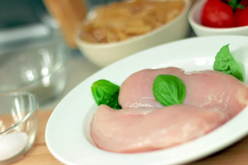 Close-up of raw chicken breasts on a plate with basil leaves, ideal for culinary themes.