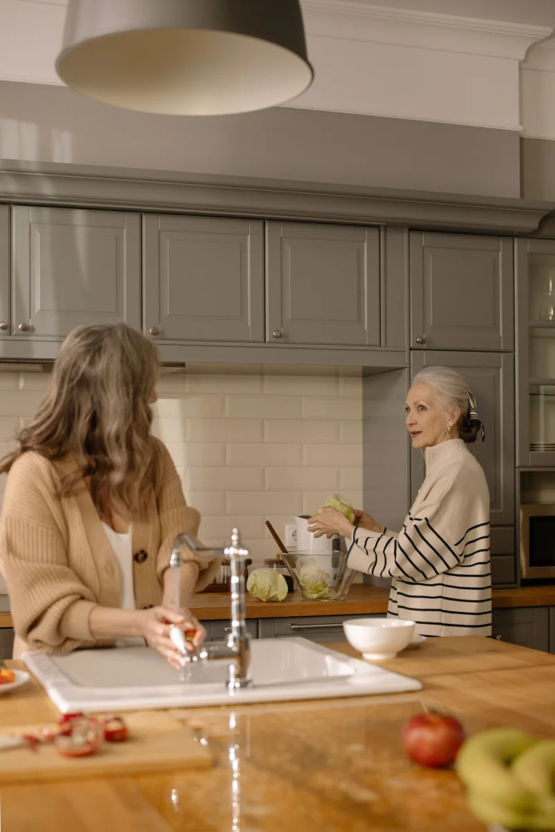 Senior women preparing a meal and conversing in a modern kitchen setting.