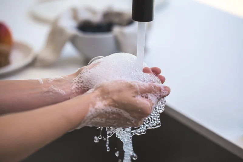Close-up of hands being washed with foamy soap under a faucet, highlighting hygiene and cleanliness.
