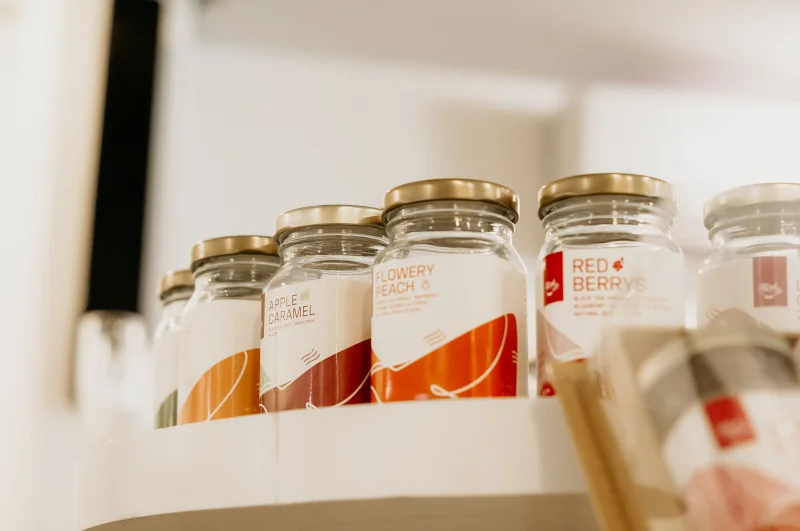 Glass jars with various labels on a shelf display in a store setting.