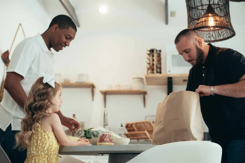 A family of three cheerfully unpacks groceries in a stylish, modern kitchen setting.
