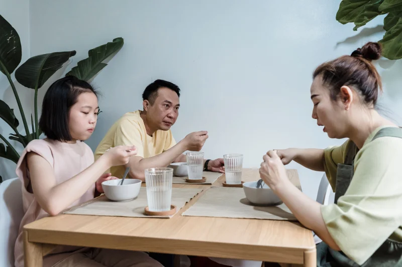 Asian family seated at dining table enjoying breakfast together indoors.