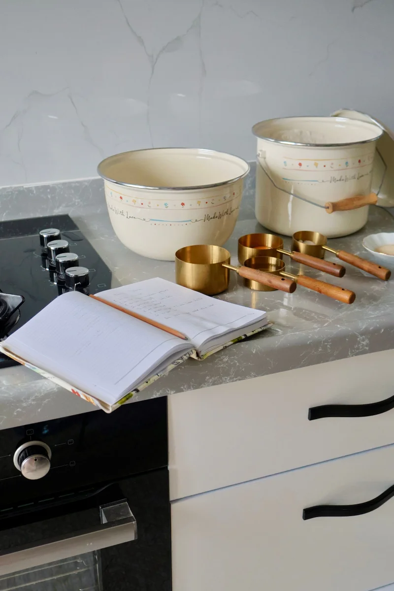 Light-filled kitchen with mixing bowls, measuring cups, and an open cookbook.