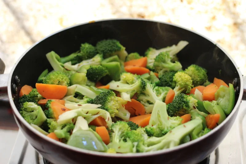 Close-up of broccoli and carrots in a frying pan, showcasing healthy home cooking.