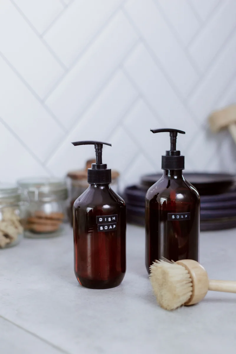 Minimalist kitchen setting featuring dish soap dispensers and cleaning brush on countertop.