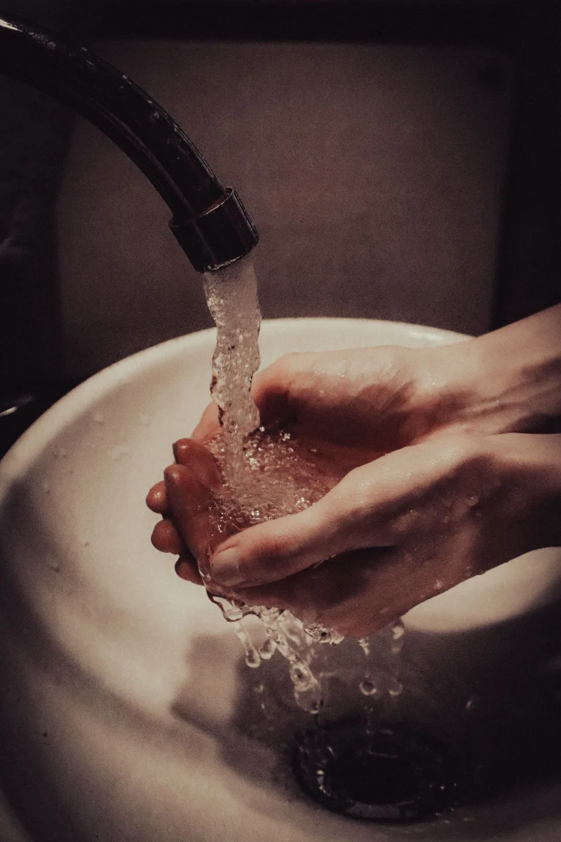 Close-up of hands being washed under a faucet in a bathroom.