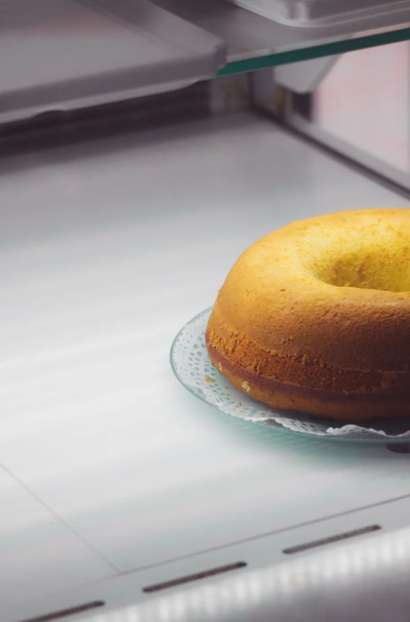 A freshly baked bundt cake displayed on a lace plate inside a refrigerator.