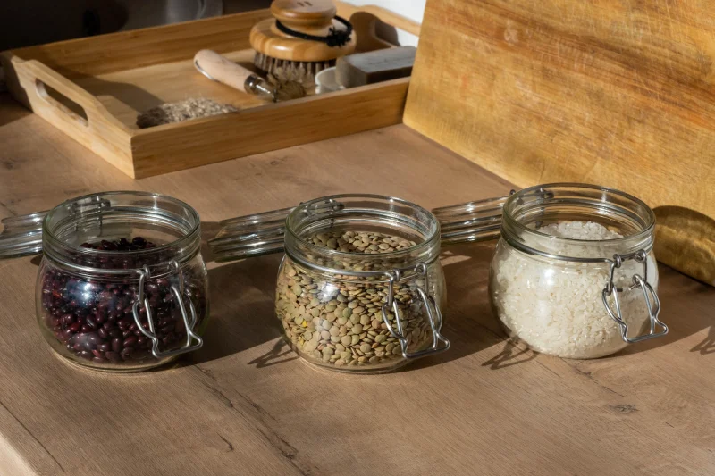 Glass jars of beans, lentils, and uncooked rice on a wooden table with warm lighting.