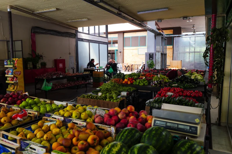 Indoor market showcasing a colorful array of fresh fruits and vegetables with customers in the background.