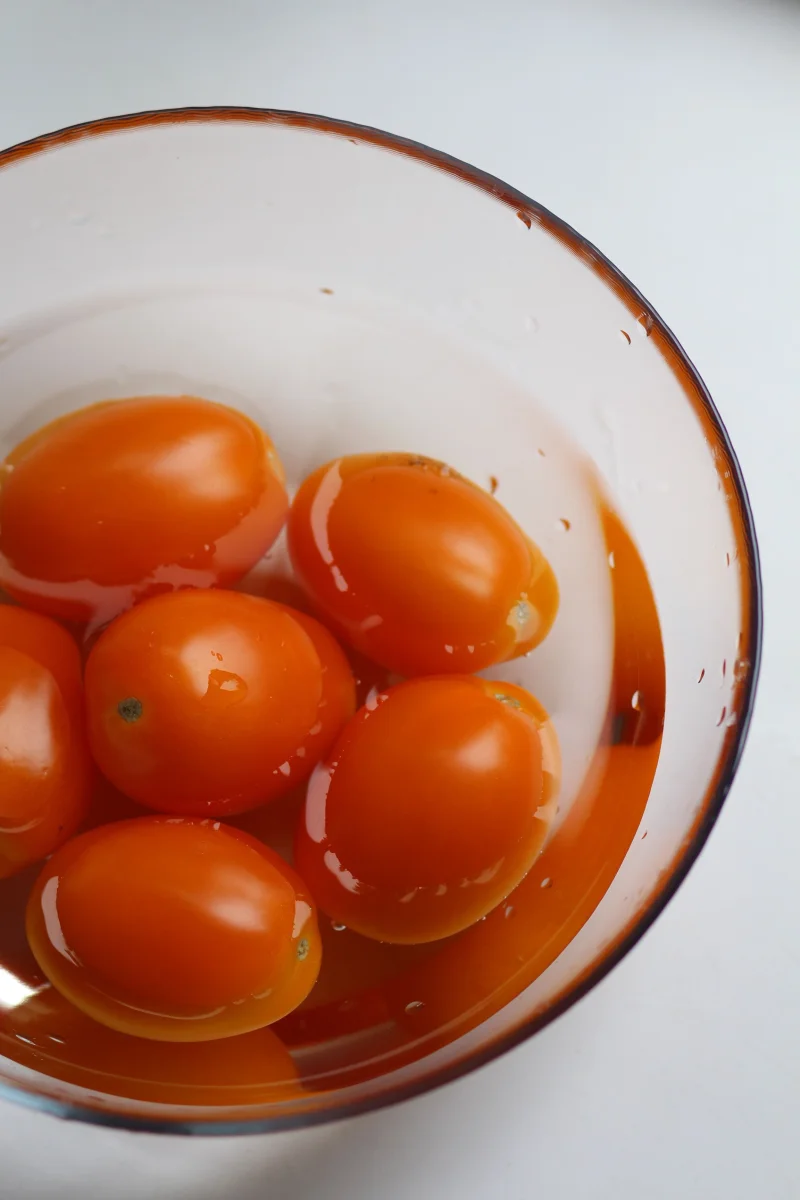 Close-up of fresh cherry tomatoes soaking in water in a transparent bowl on white background.