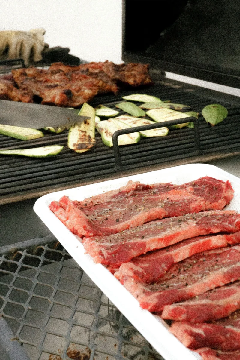 Close-up of seasoned steaks and vegetables grilling outdoors in Chihuahua, Mexico.