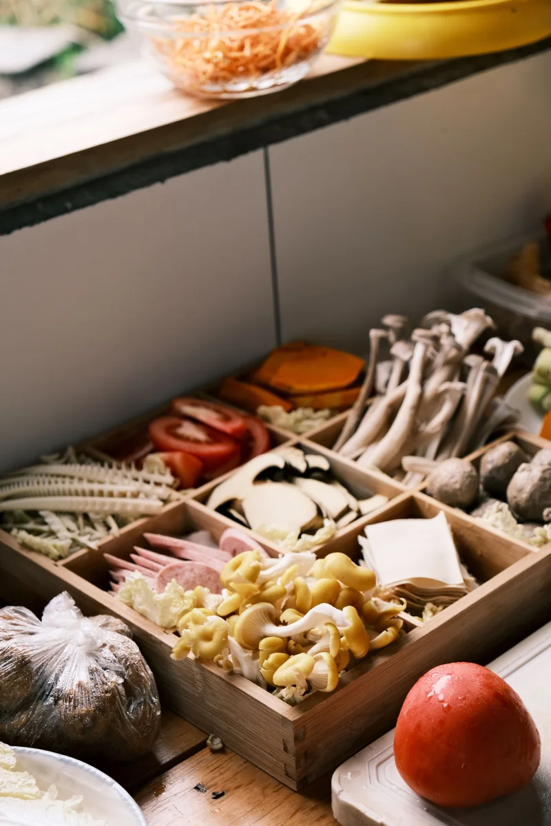 A variety of fresh vegetables and mushrooms displayed in a wooden box on a kitchen counter.