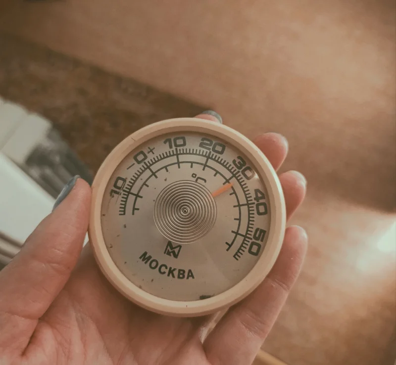 Close-up of a hand holding a vintage Moscow thermometer displaying temperature.