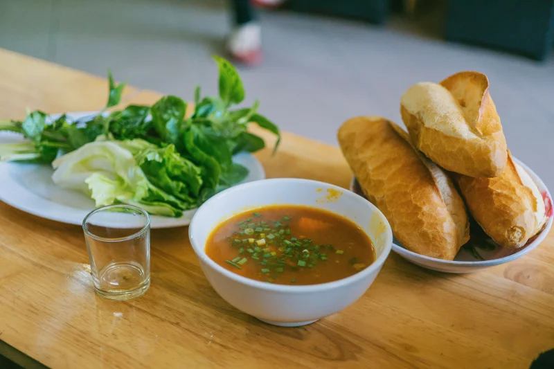A bowl of flavorful Vietnamese soup accompanied by fresh greens and crusty baguette.
