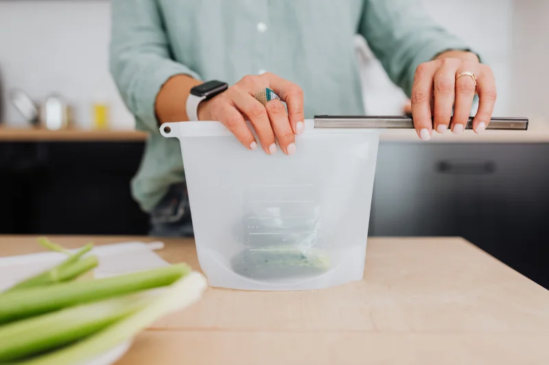 Woman sealing a reusable silicone storage pouch in a kitchen setting.