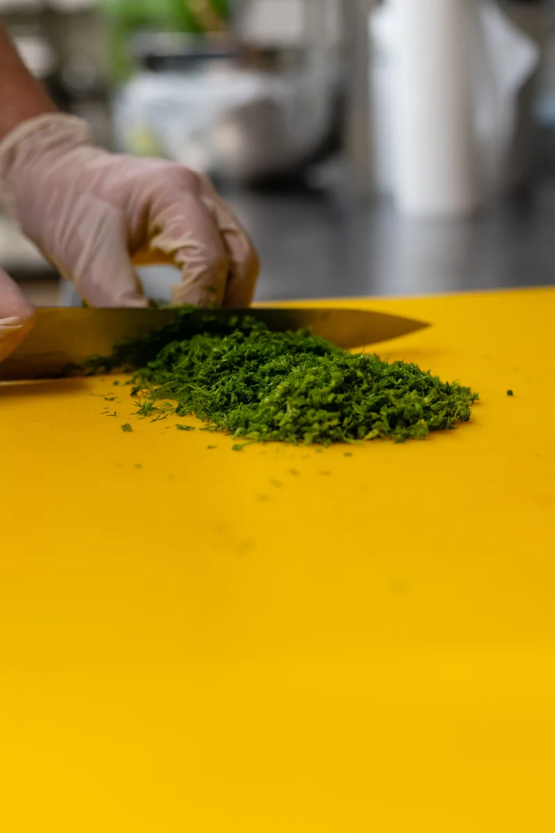 A detailed shot of fresh herbs being chopped on a bright yellow cutting board.