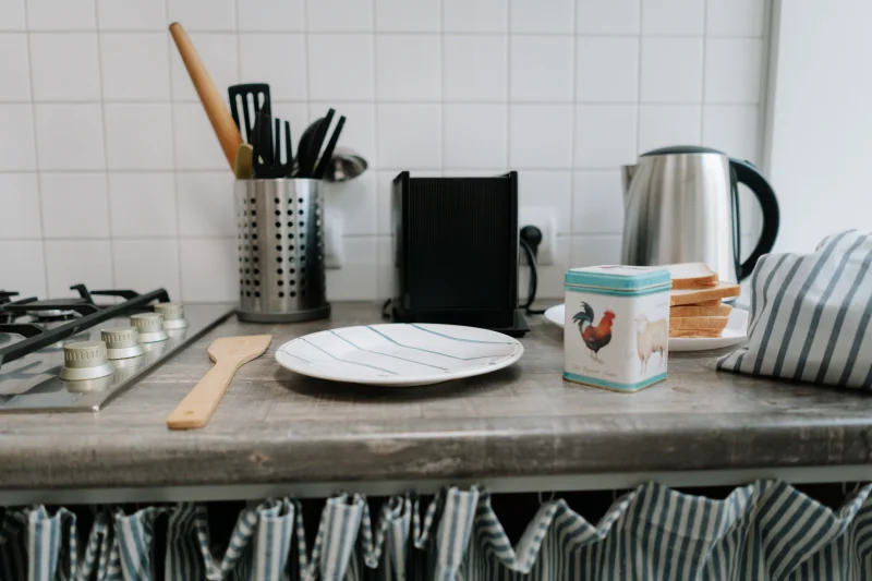 A clean kitchen counter featuring utensils, a kettle, and a tin can with vibrant design.