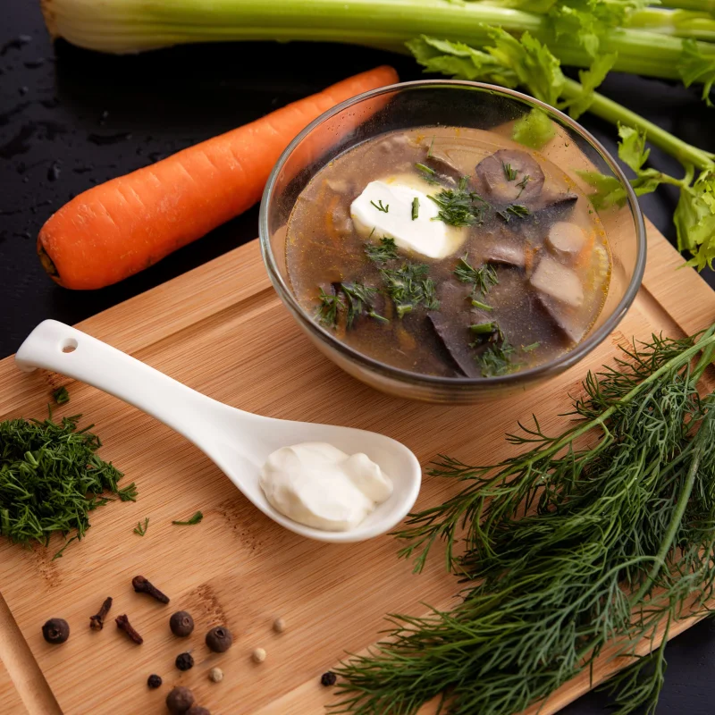 A flavorful mushroom soup garnished with cream and herbs, surrounded by fresh vegetables and spices.