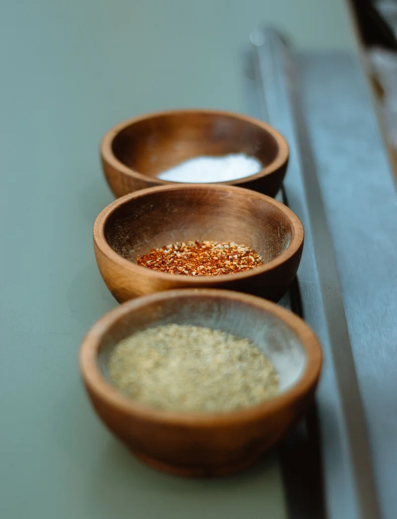 An artistic close-up of salt, pepper, and chili flakes in wooden bowls.