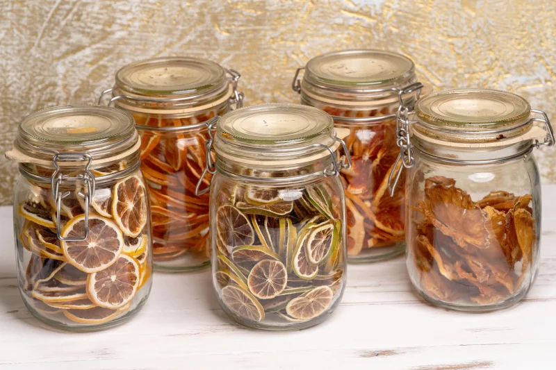 Colorful, preserved dried fruits arranged neatly in decorative glass jars on a white surface.