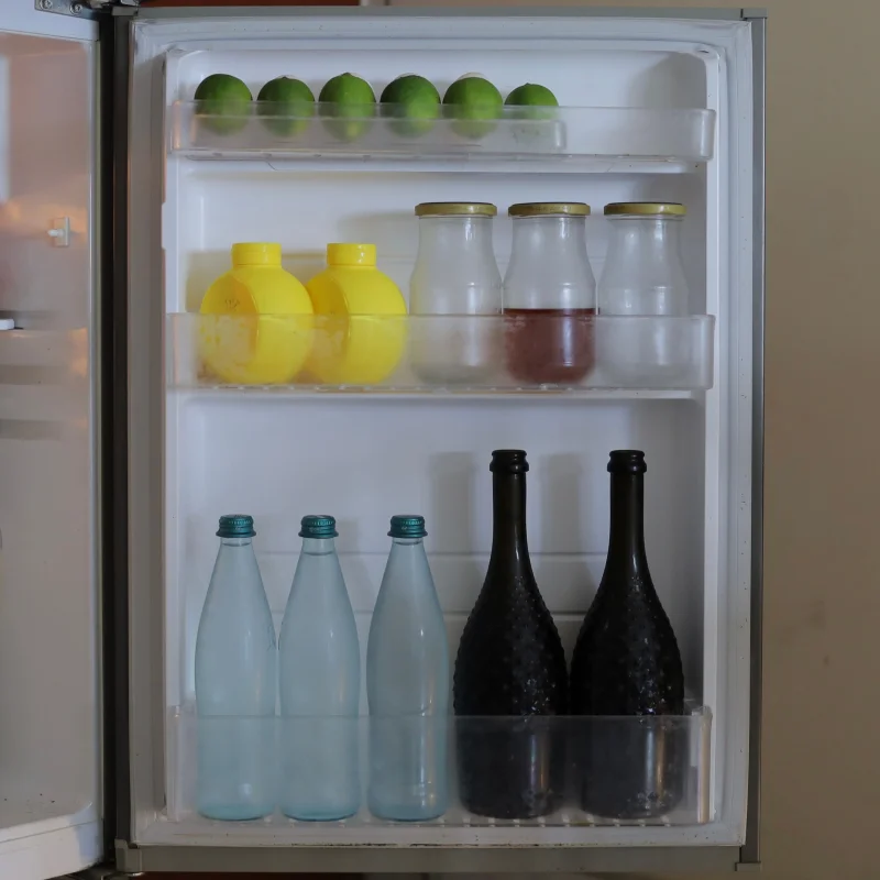 An open fridge displaying bottles, limes, and lemon-shaped containers.