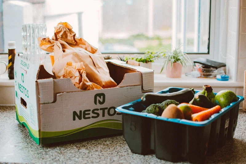 A variety of fresh fruits and vegetables in cartons on a kitchen counter in natural light.