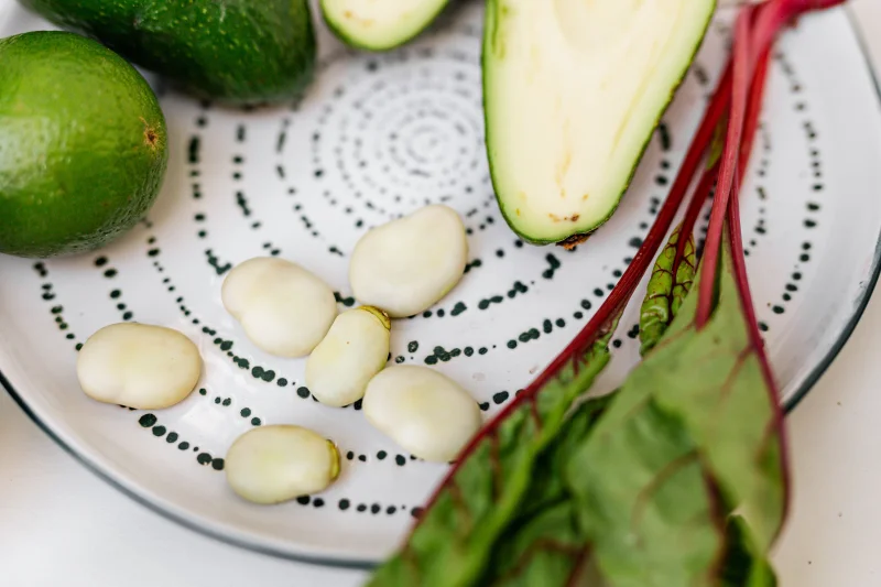Close-up of fresh avocado, beans, and greens on a decorative plate.