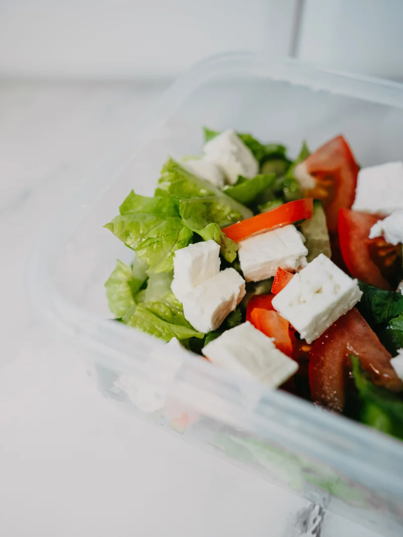 A fresh garden salad with feta cheese in a plastic container, perfect for a healthy meal.