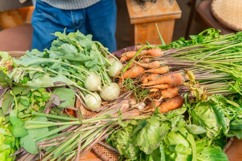 A colorful display of fresh, organic vegetables including carrots and turnips on a wooden table.