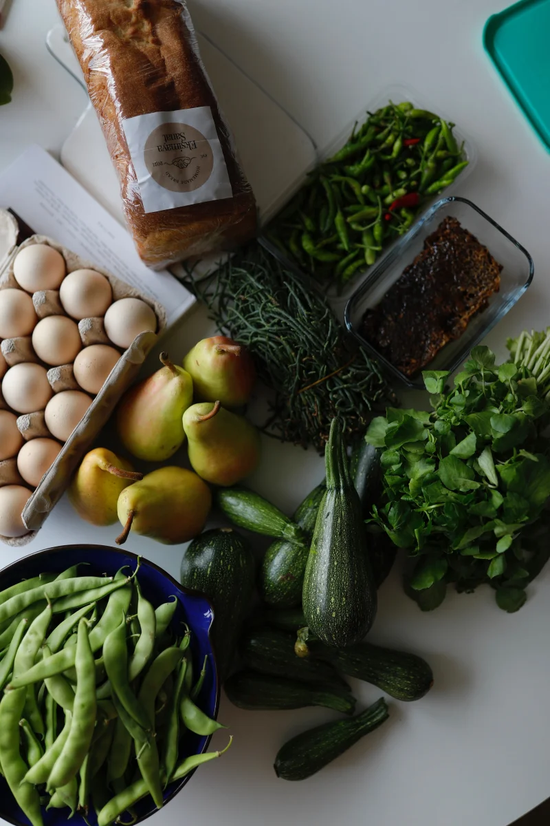 A variety of fresh vegetables, pears, eggs, and bread on a white background.