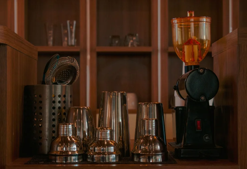 Organized bar equipment including shakers and a coffee grinder on wooden shelves.