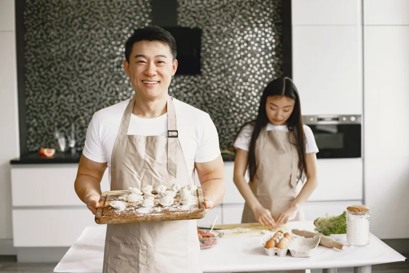 Asian couple making dumplings in a contemporary kitchen, smiling and enjoying their time together.
